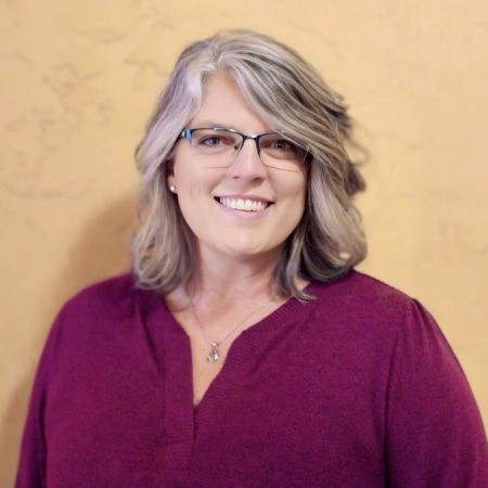 Denise Busch, Parament Real Estate - Headshot 40-something woman with glasses and salt and pepper medium  length hair in burgundy red sweater